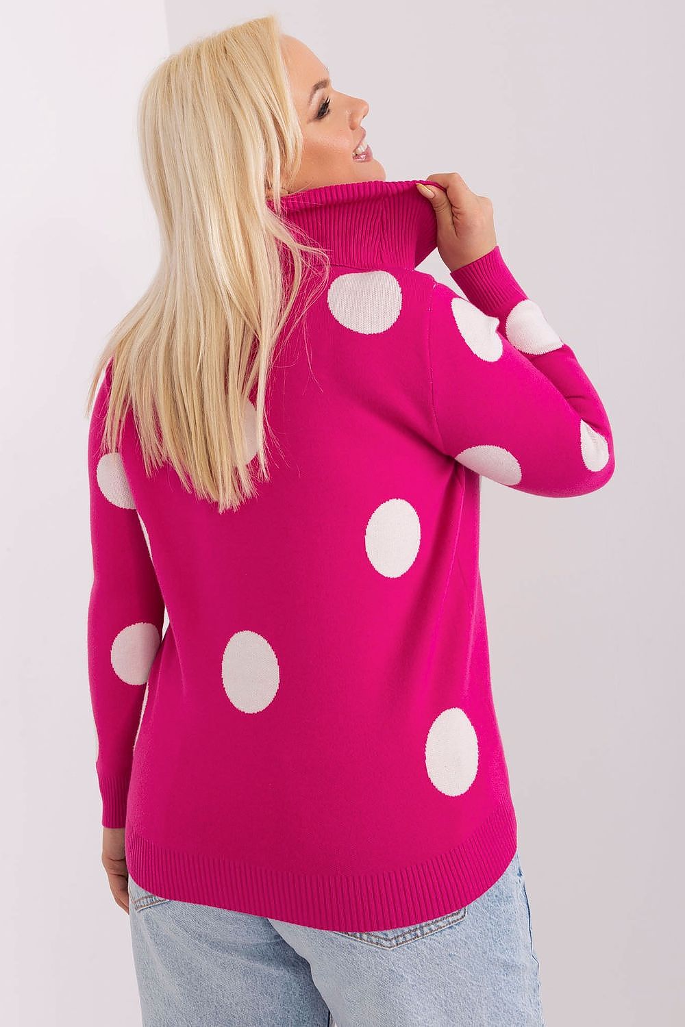Woman wearing a bright pink sweater with white polka dots against a plain background