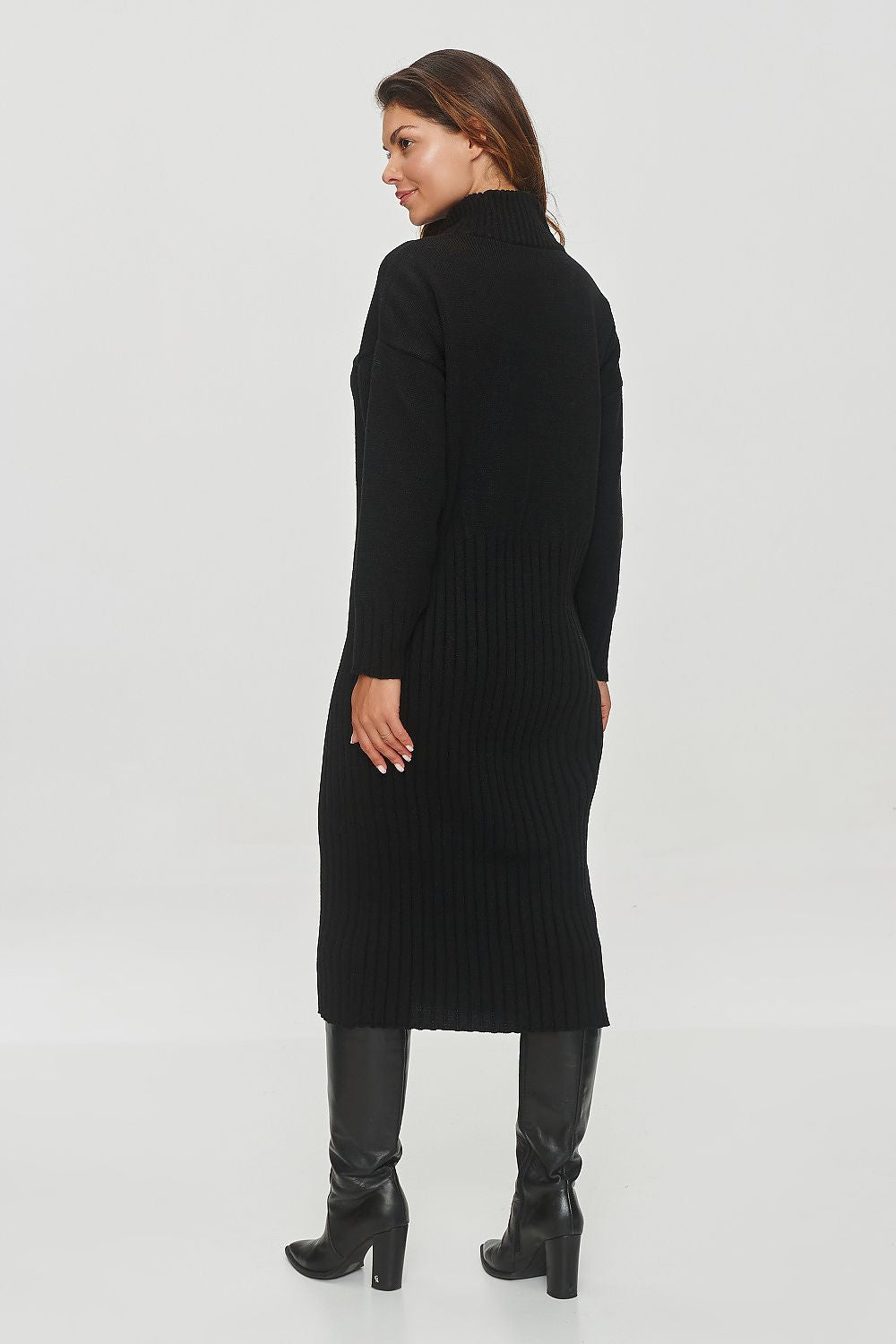 Woman wearing a long black ribbed dress with knee-high black boots on a white background