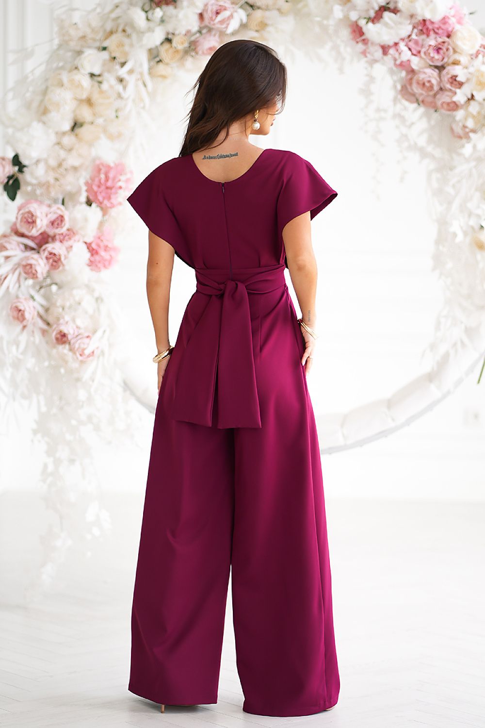 Woman wearing a burgundy jumpsuit with a floral background
