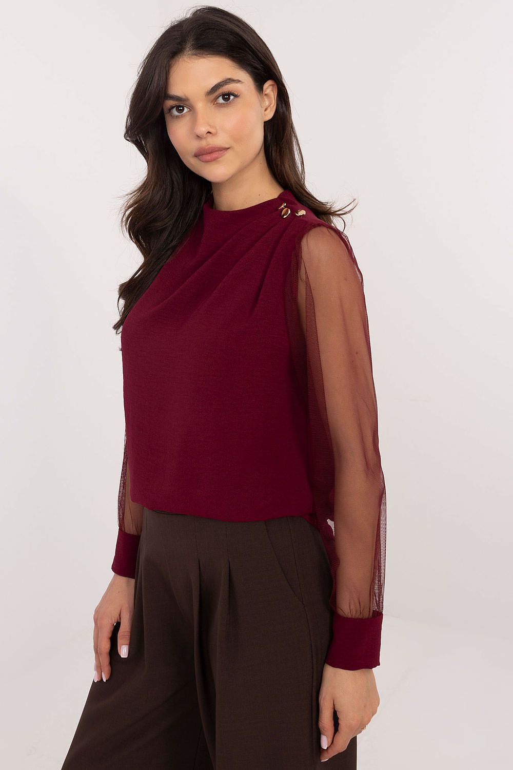 Woman wearing a burgundy top with sheer sleeves on a white background