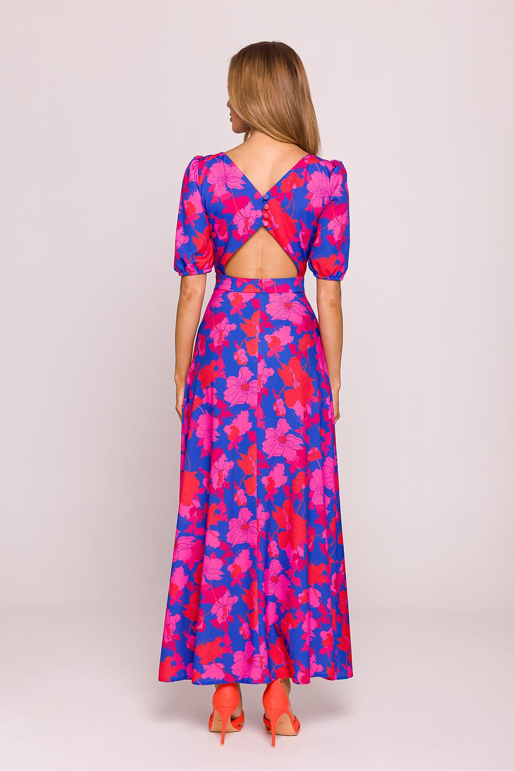 Woman wearing a colorful floral dress with a cutout back on a light pink background