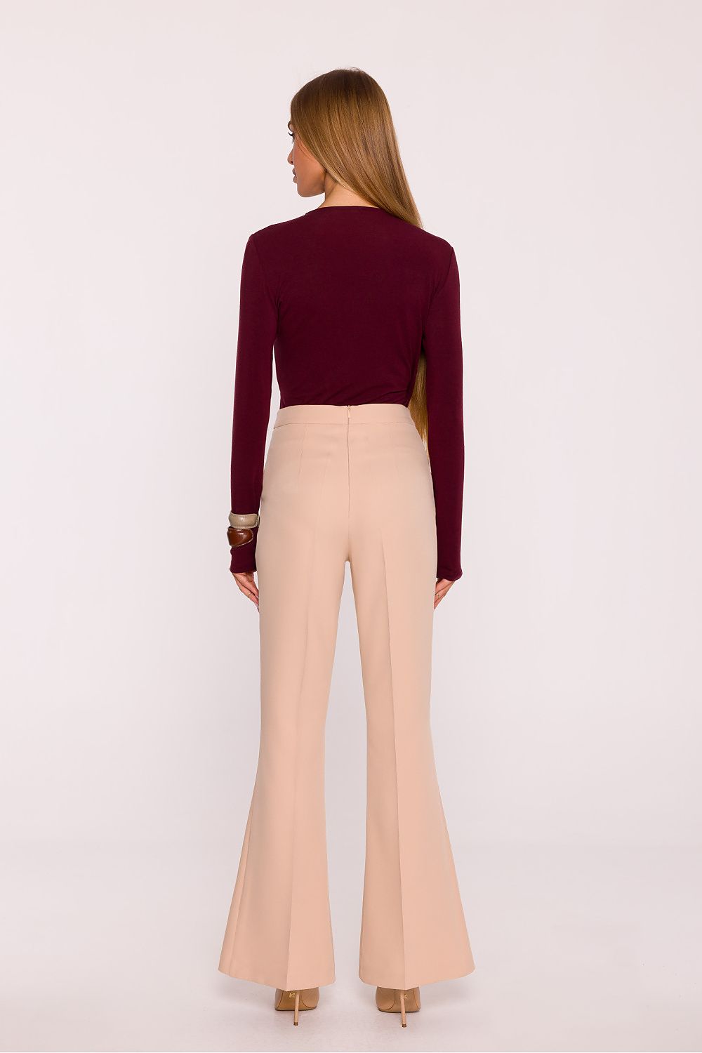 Woman wearing a burgundy sweater and beige flared pants on a white background