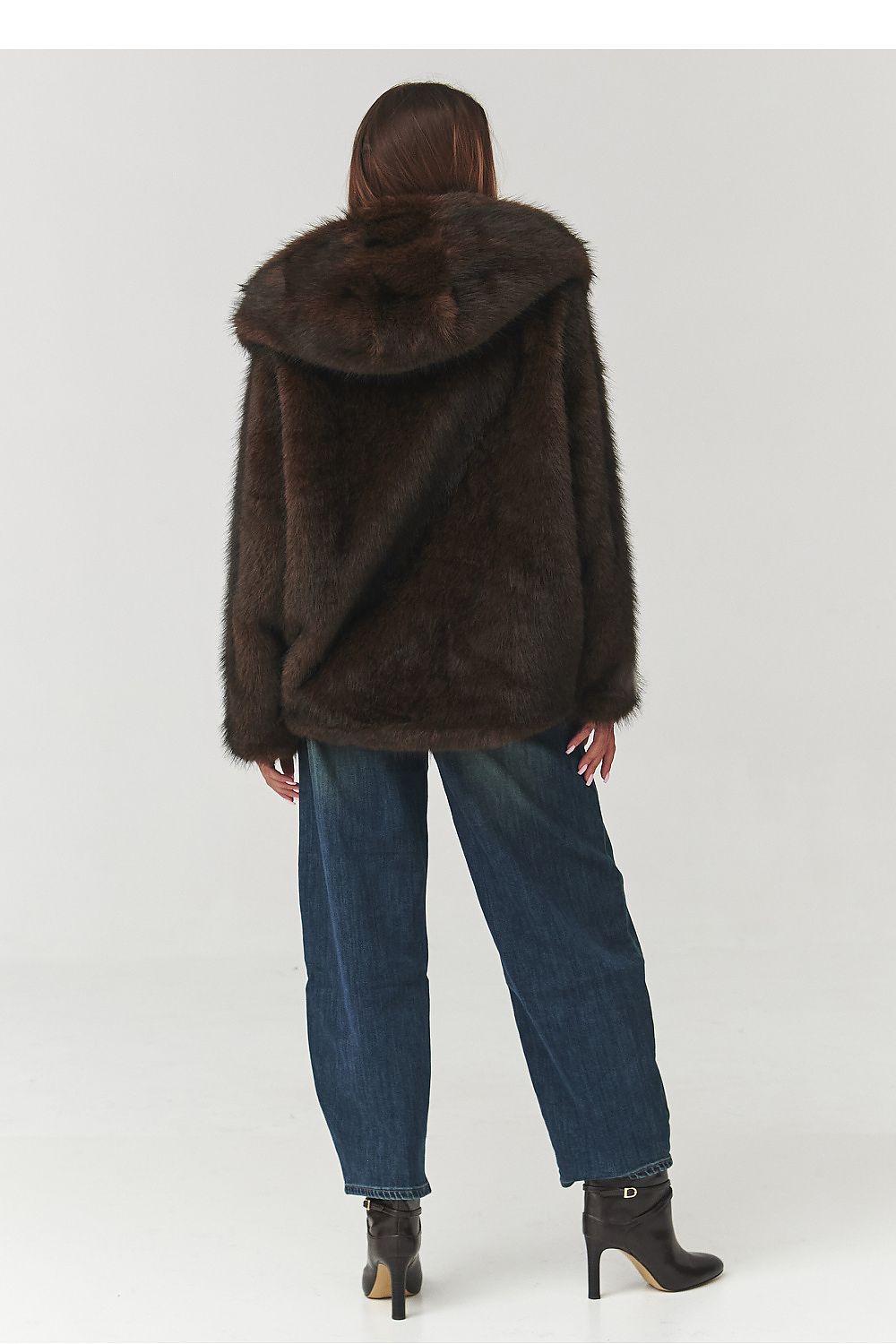 Person wearing a brown fur coat and blue jeans on a white background