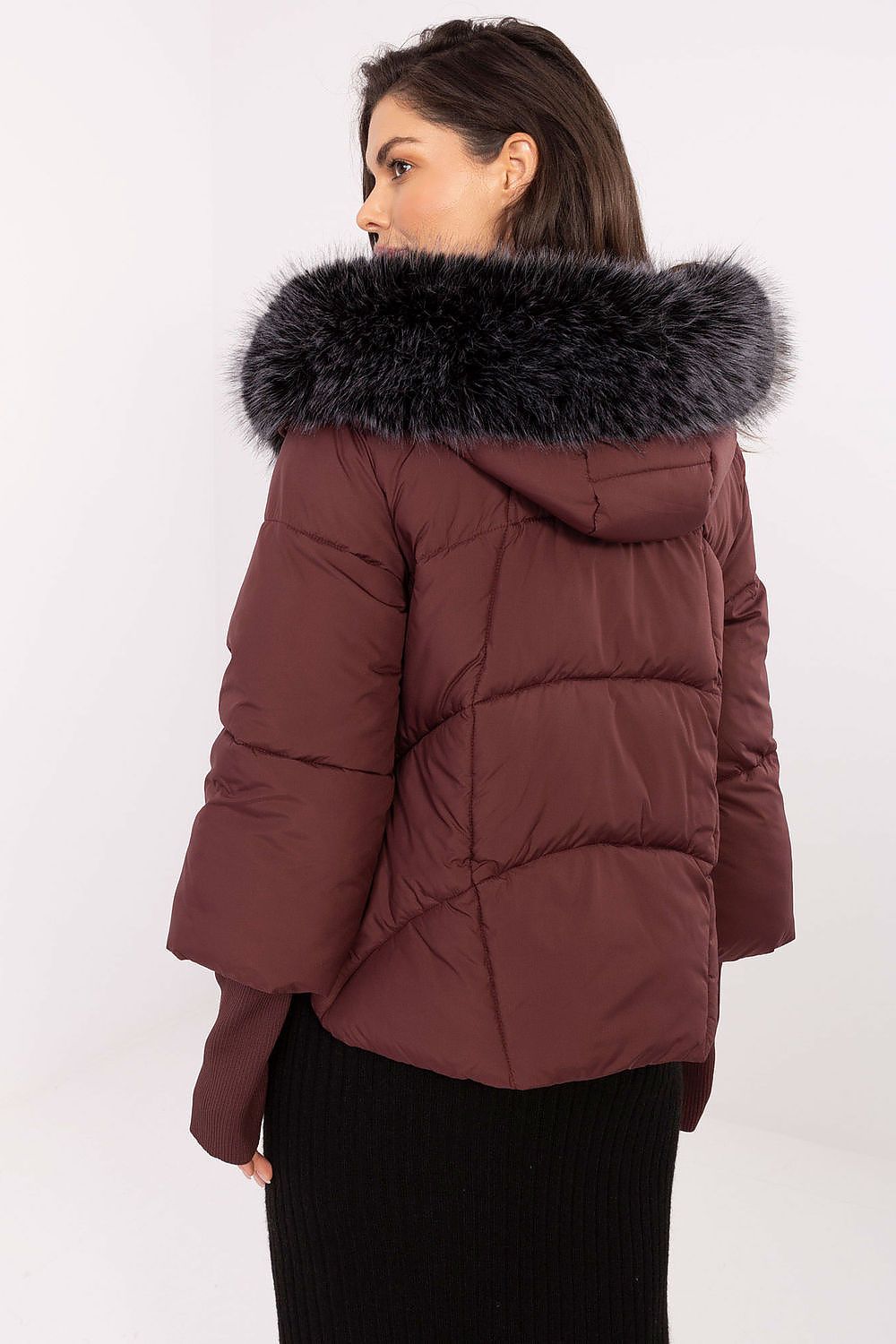 Woman wearing a brown puffer jacket with a fur-lined hood on a white background