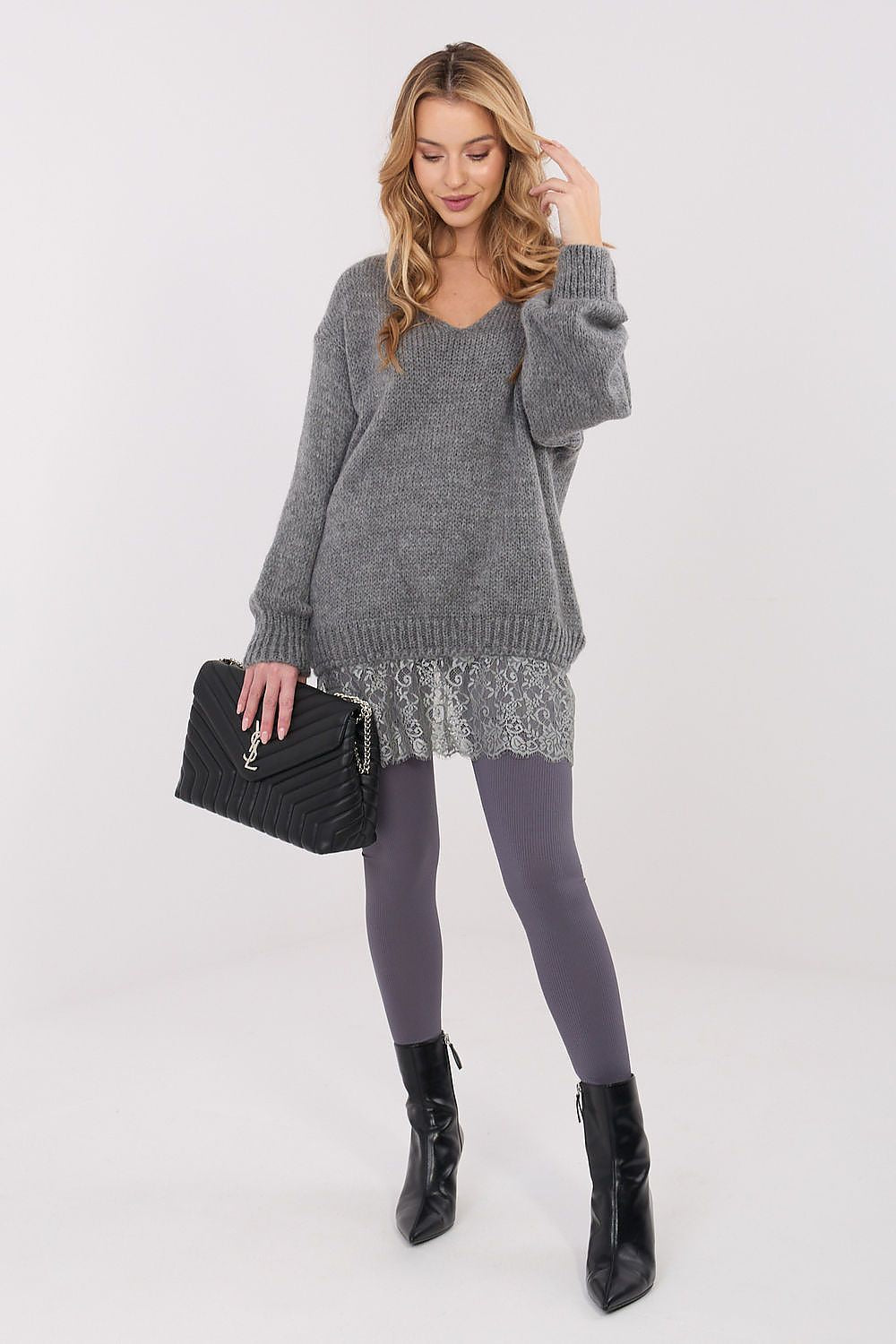 Woman wearing a gray sweater over a dress with black boots and a black handbag on a white background