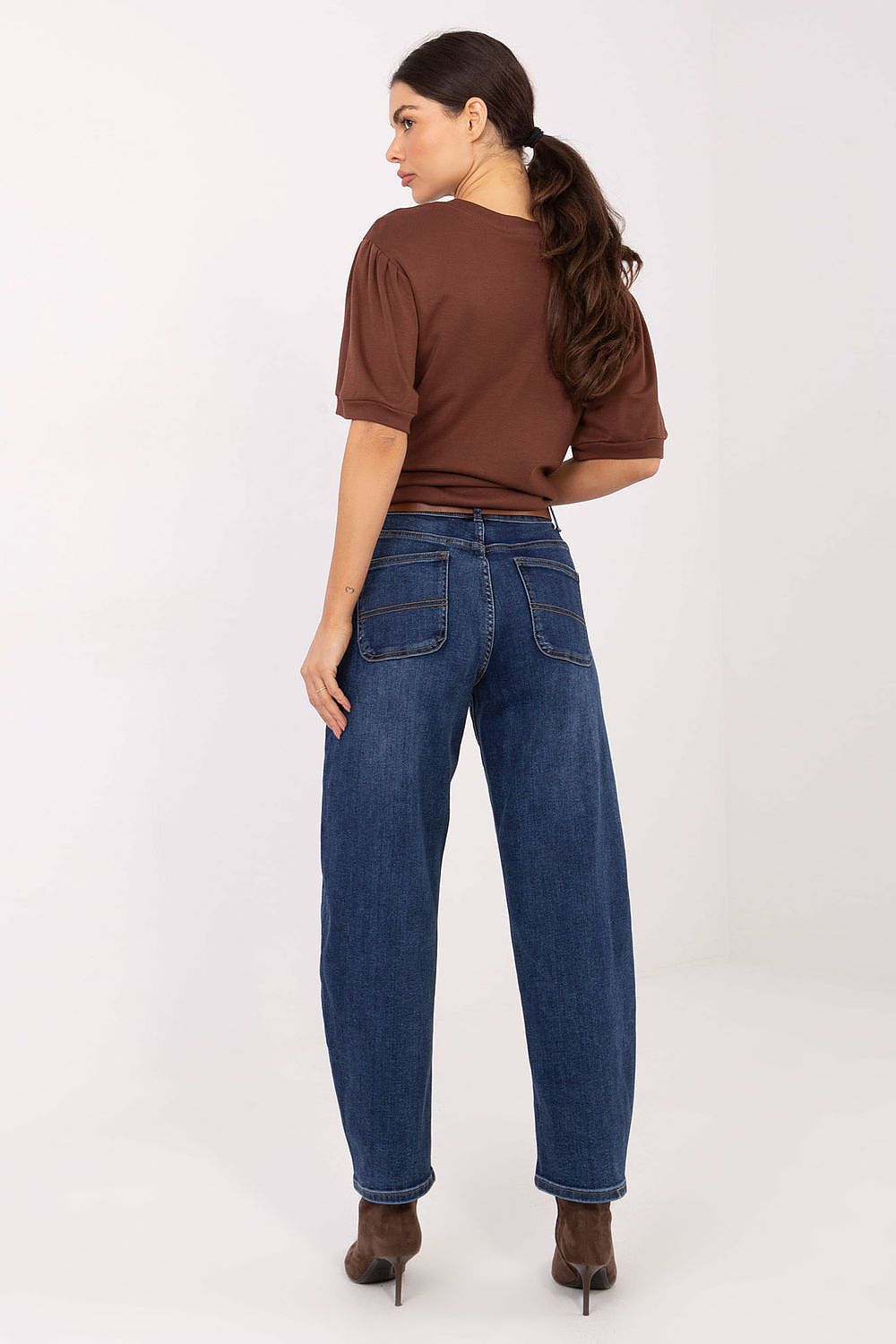 Woman wearing blue jeans and a brown top on a white background