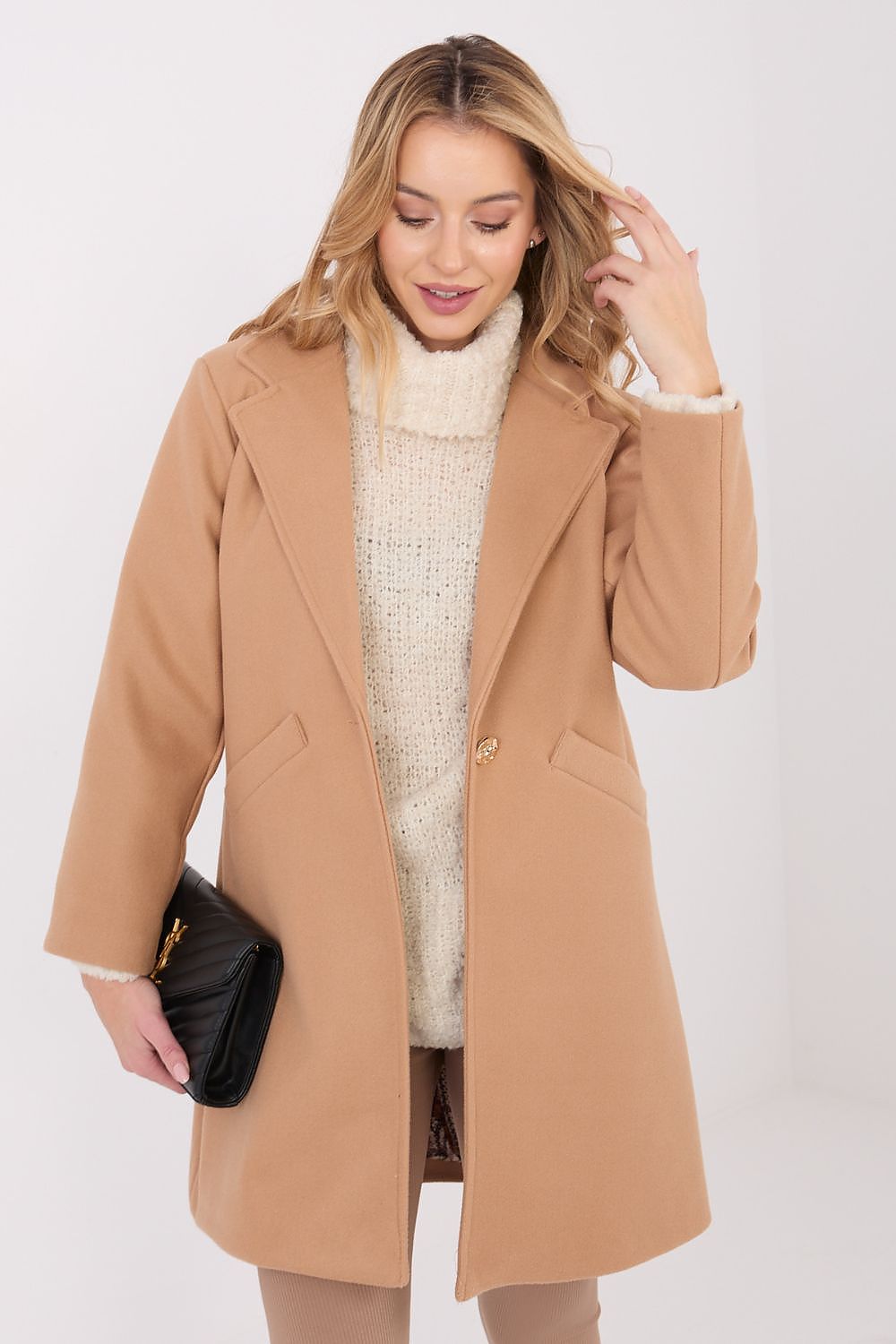 Woman wearing a beige coat over a white sweater on a white background