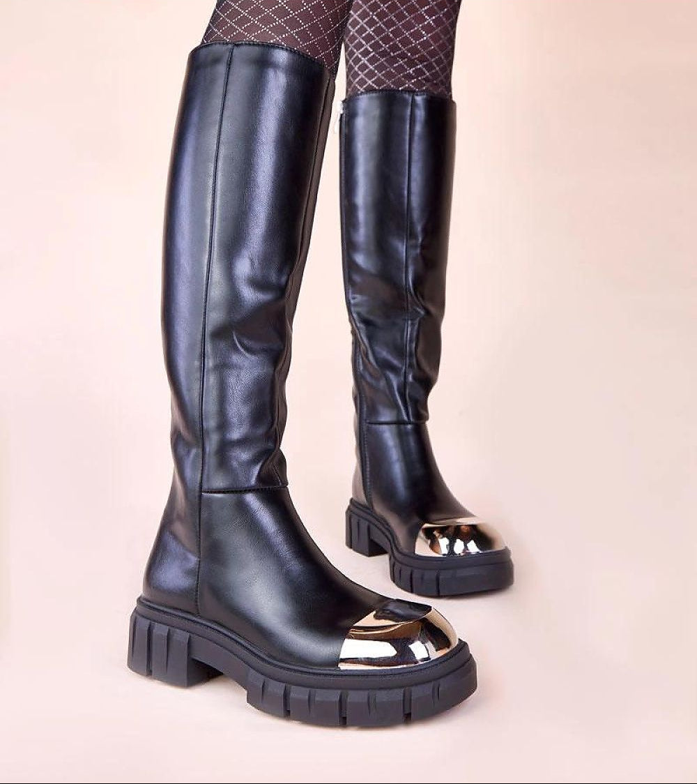 Black knee-high boots with metallic sole on a beige background