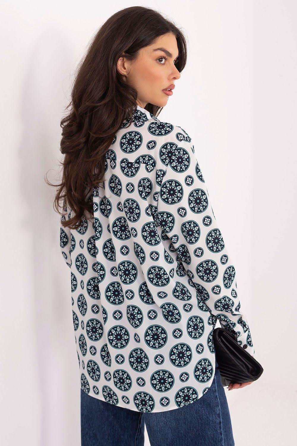 Woman wearing a white blouse with black floral pattern against a plain background