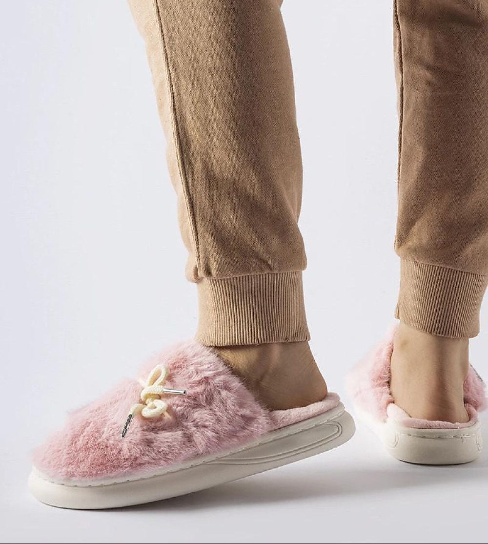 Pink fuzzy slippers worn with beige pants on a light gray background
