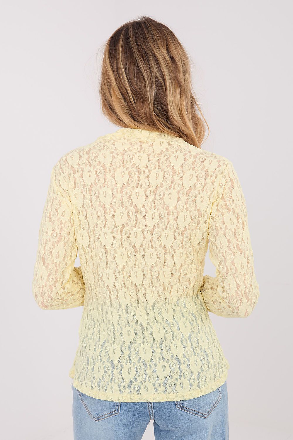 Woman wearing a light yellow textured sweater on a plain background