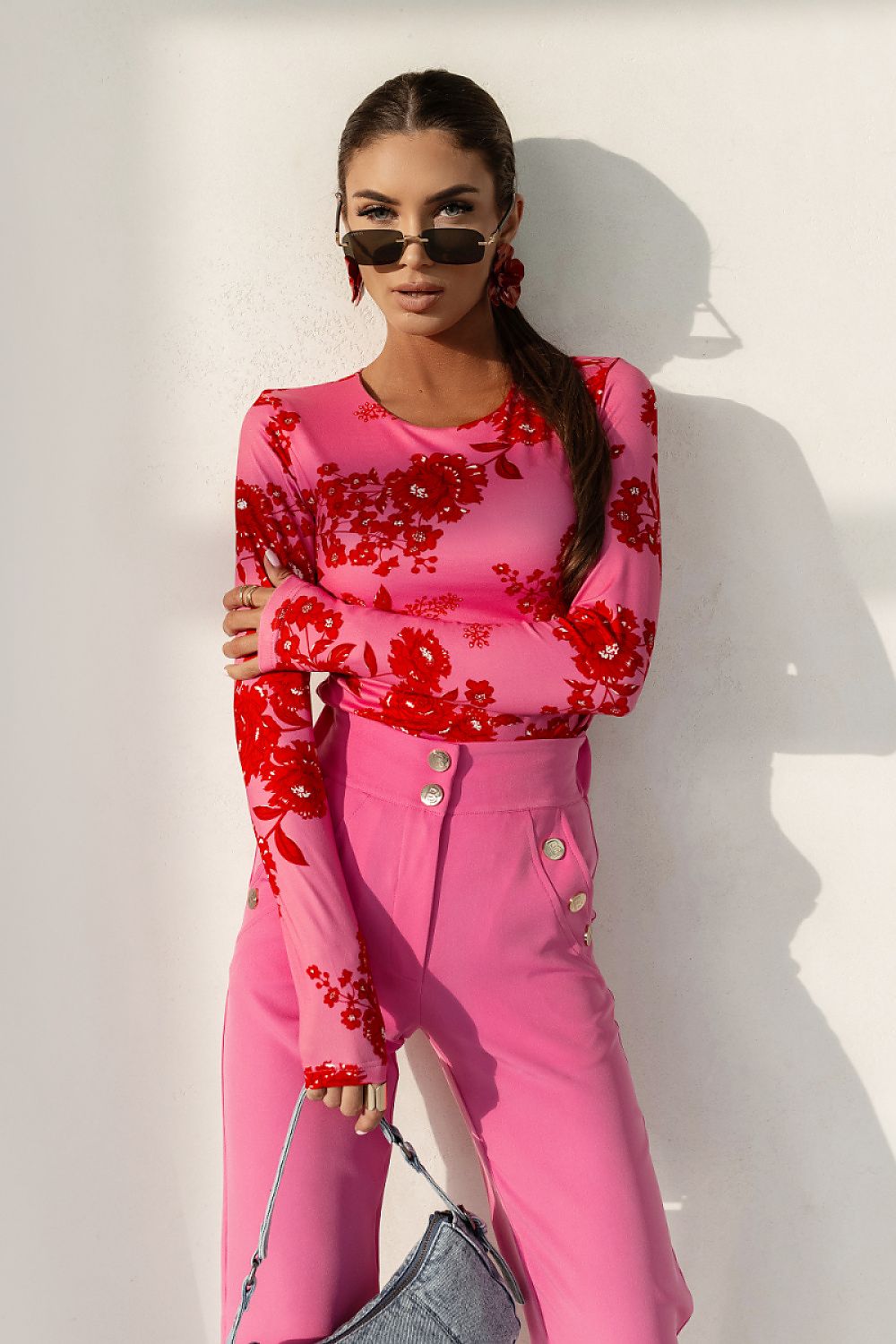 Woman in a pink outfit with red floral patterns against a white background