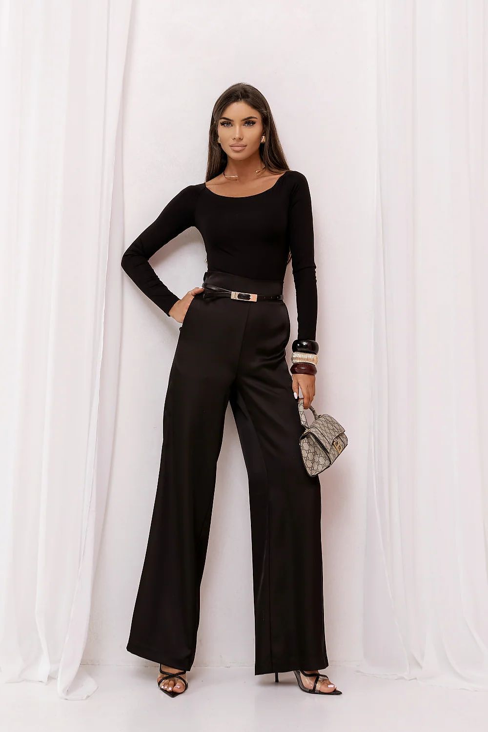 Woman in a black outfit with wide-leg pants against a white curtain background