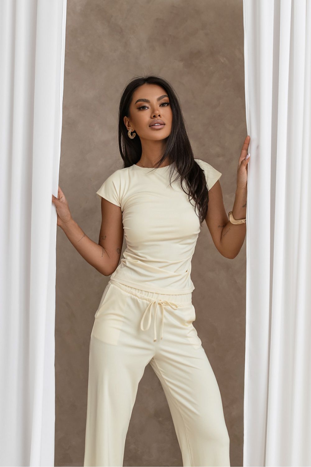 Woman wearing a light-colored outfit standing against a neutral background