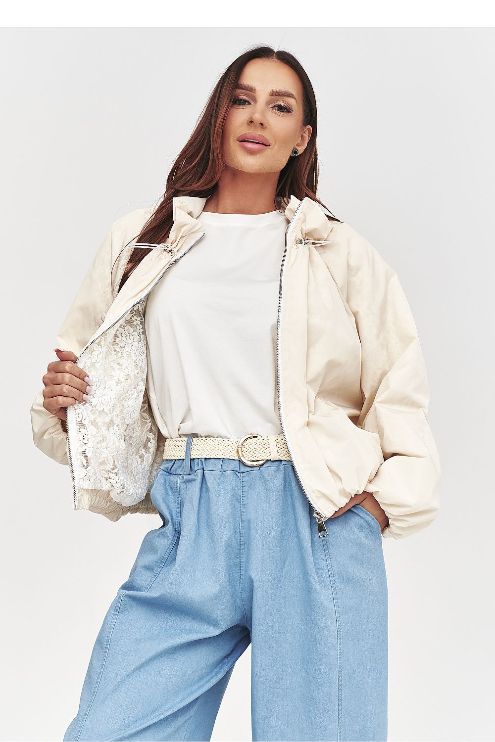 Woman wearing a beige jacket, white shirt, and blue pants on a light gray background