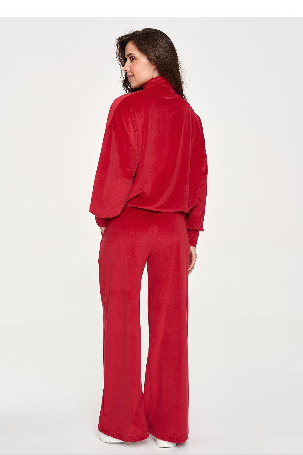 A woman wearing a matching red velour tracksuit, featuring a cropped long-sleeve top and wide-leg pants, shown from a rear three-quarter view against a plain white studio background.