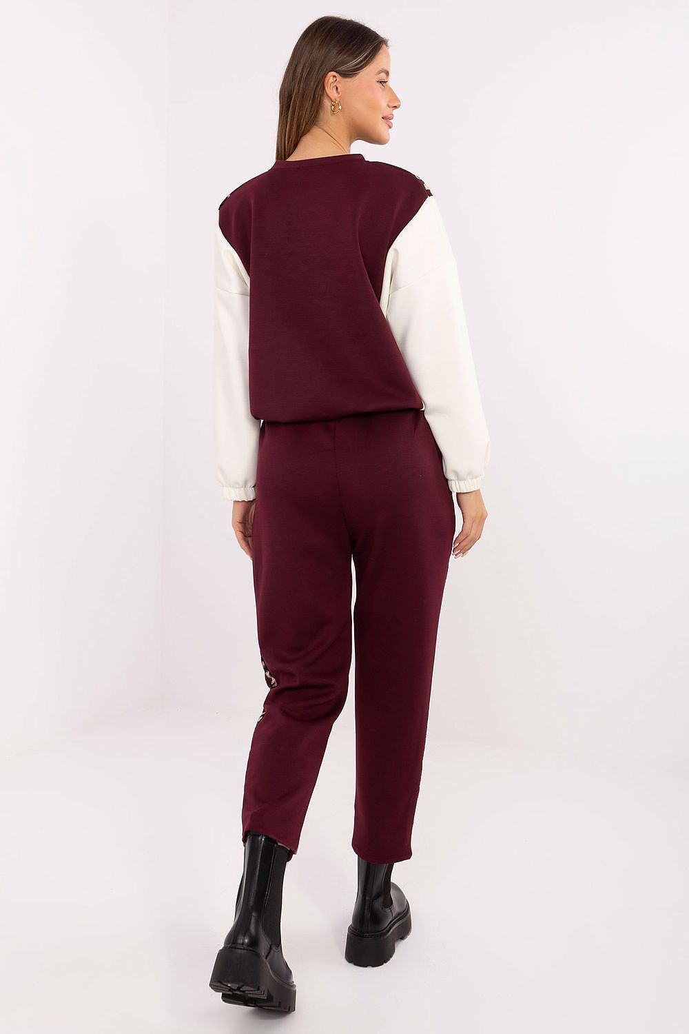 A woman shown from the back wearing a two-tone burgundy and white knit top with matching burgundy cropped pants and black boots, photographed against a plain light studio background.