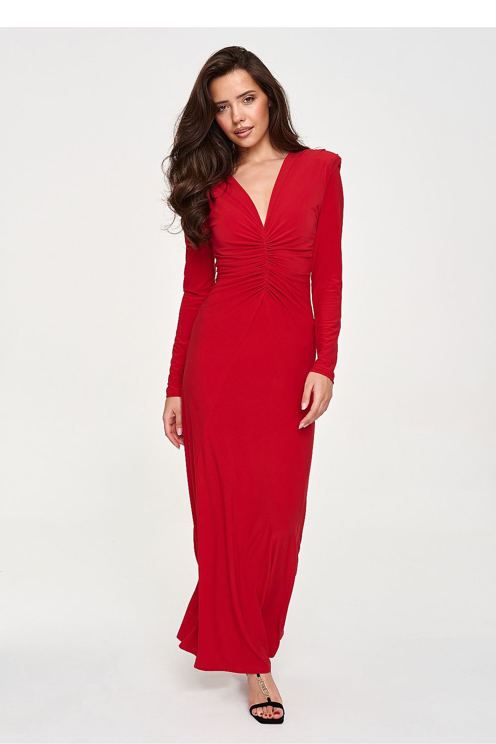 A woman modeling a long-sleeved red maxi dress with a deep V-neckline and a gathered ruched waist, set against a plain light gray studio background.