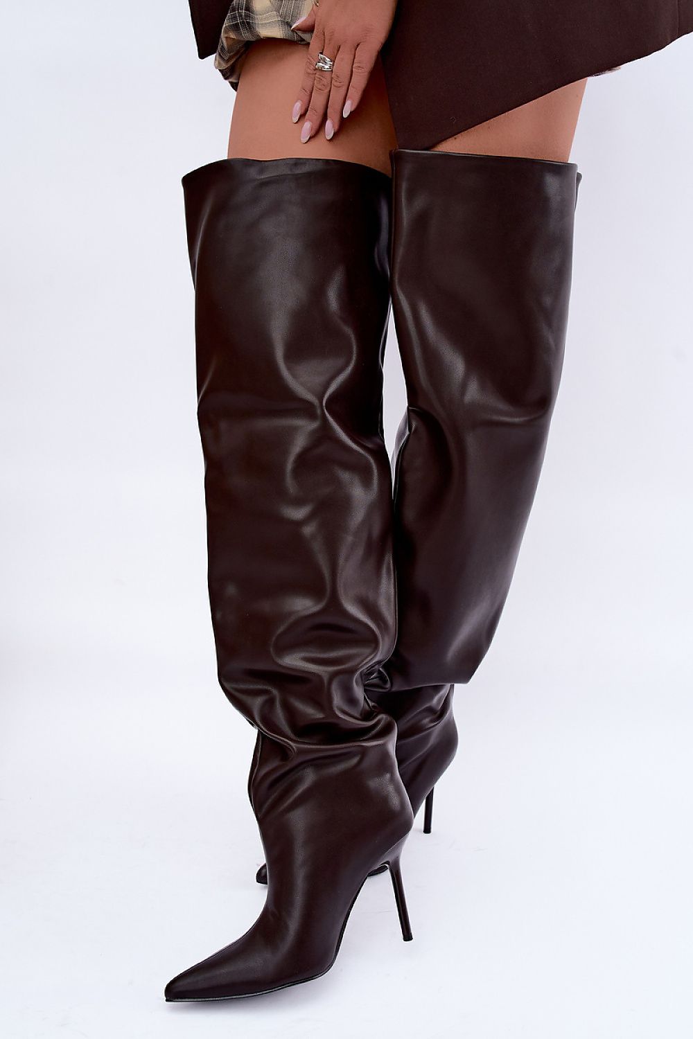 A pair of dark brown faux-leather thigh-high boots with pointed toes and slim stiletto heels, shown on a model against a white studio background.