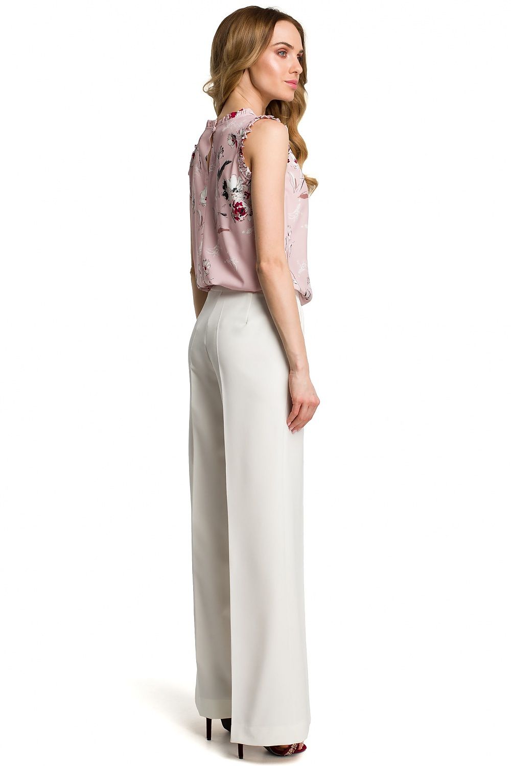 Woman wearing a floral sleeveless top and white pants on a white background