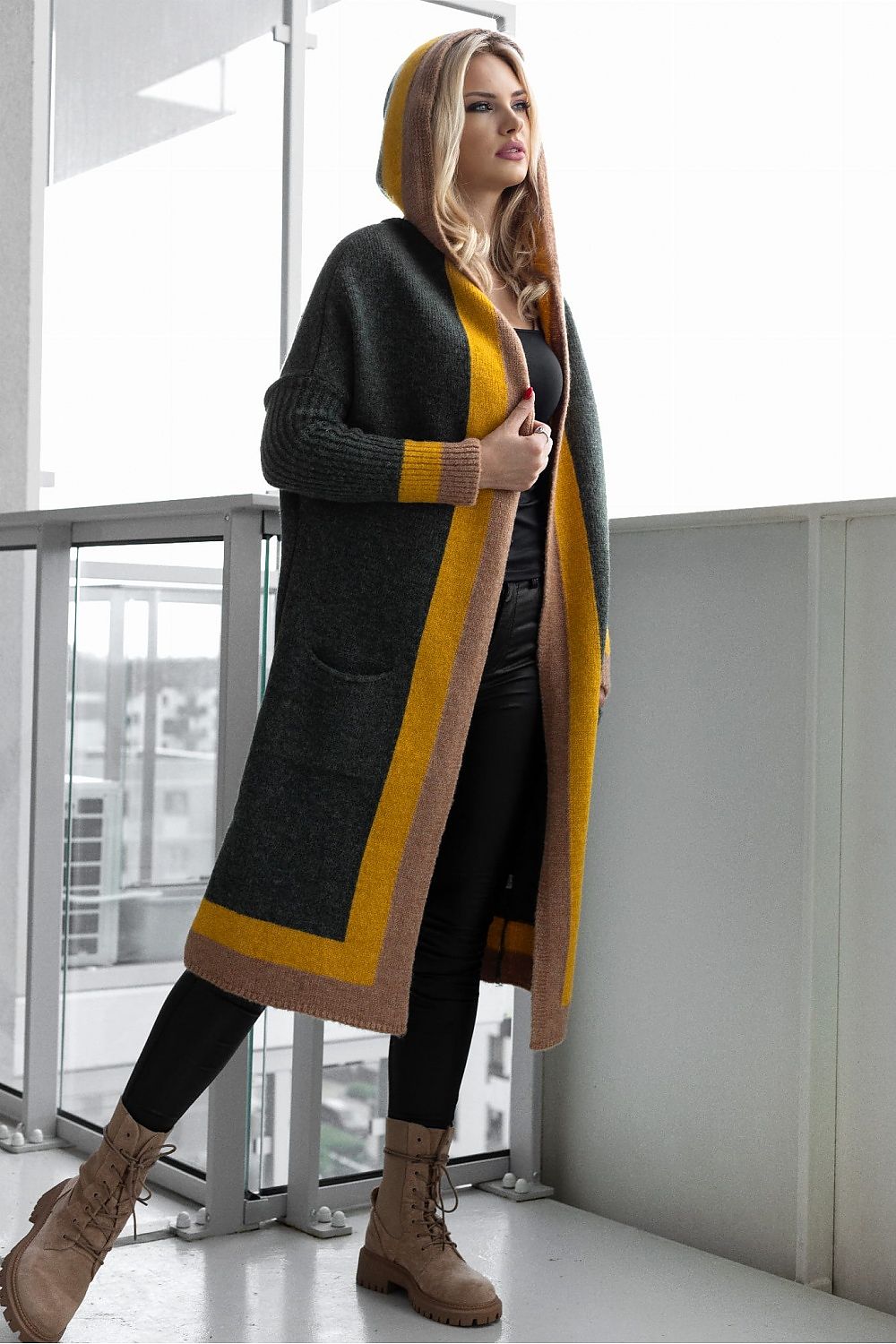 Woman wearing a long, dark green cardigan with yellow accents in an indoor setting.