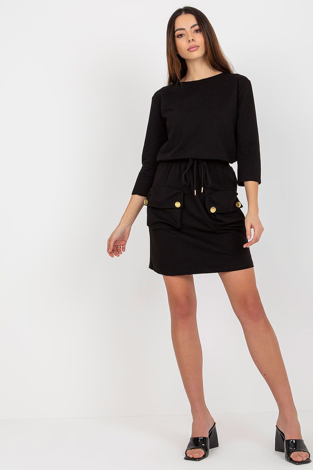 Woman wearing a black outfit with gold buttons on a white background