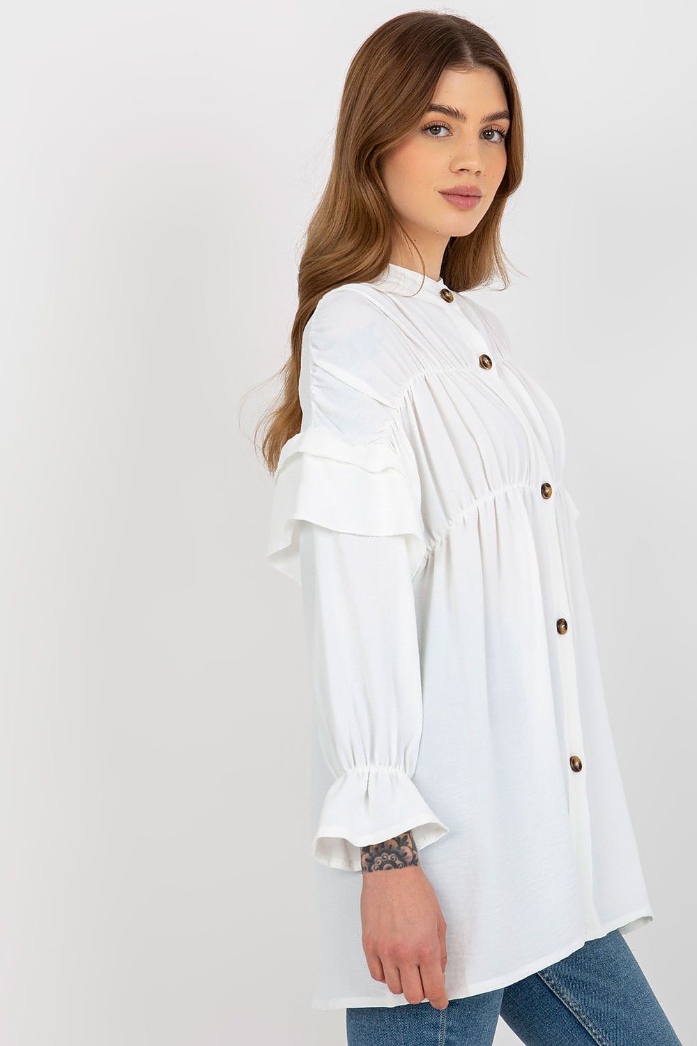 Woman wearing a white blouse with ruffled sleeves on a plain background