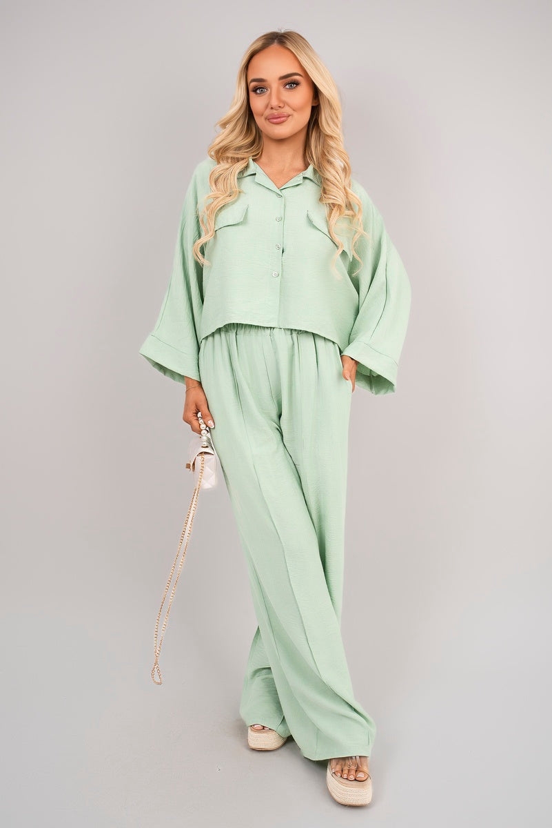 Woman wearing a light green outfit with a matching handbag on a gray background