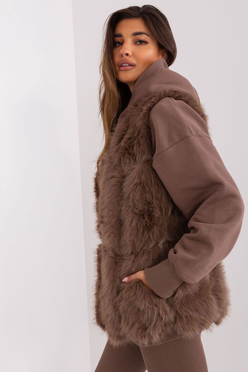 Woman wearing a brown fur vest over a matching coat on a white background