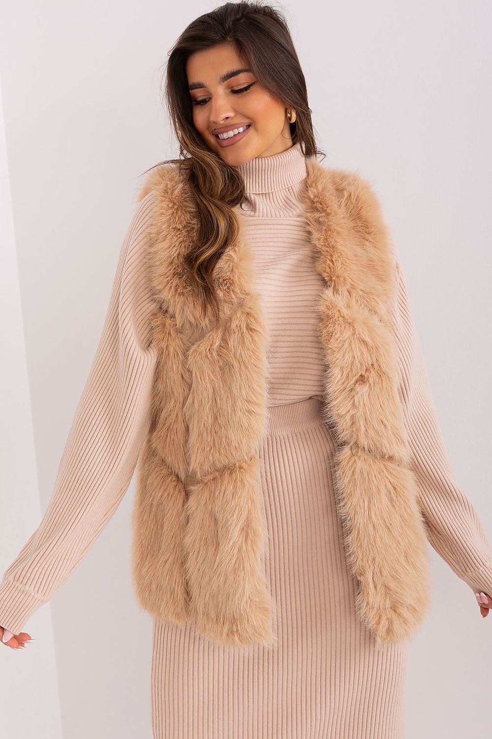 Woman wearing a beige fur vest over a matching outfit on a white background