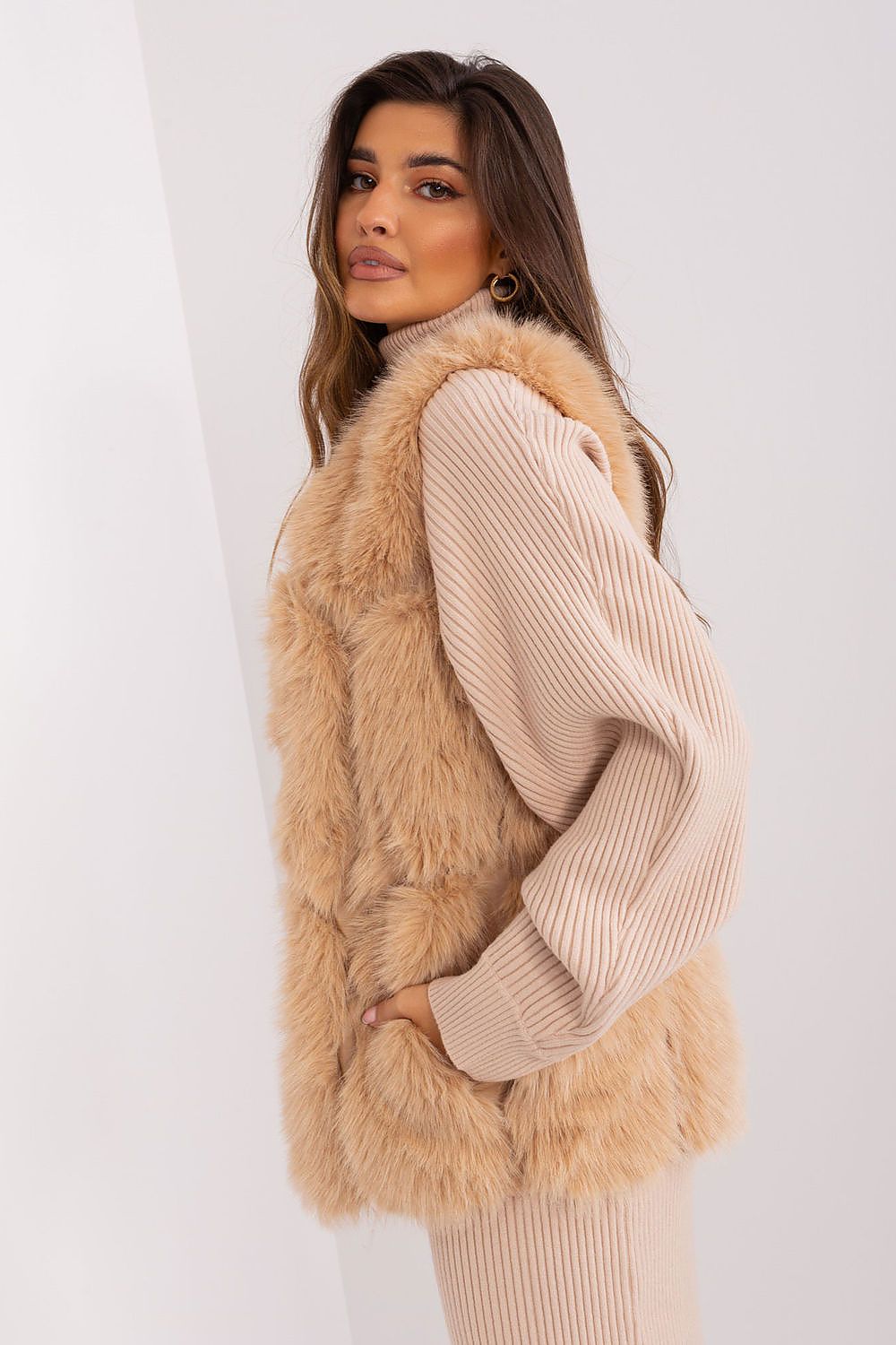 Woman wearing a beige fur vest over a beige sweater on a white background