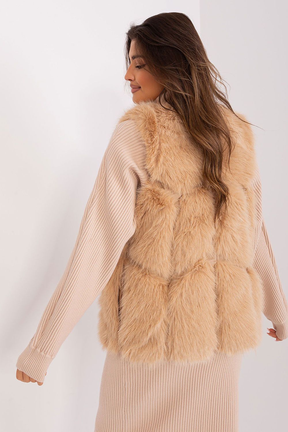 Woman wearing a beige fur vest over a matching sweater on a white background