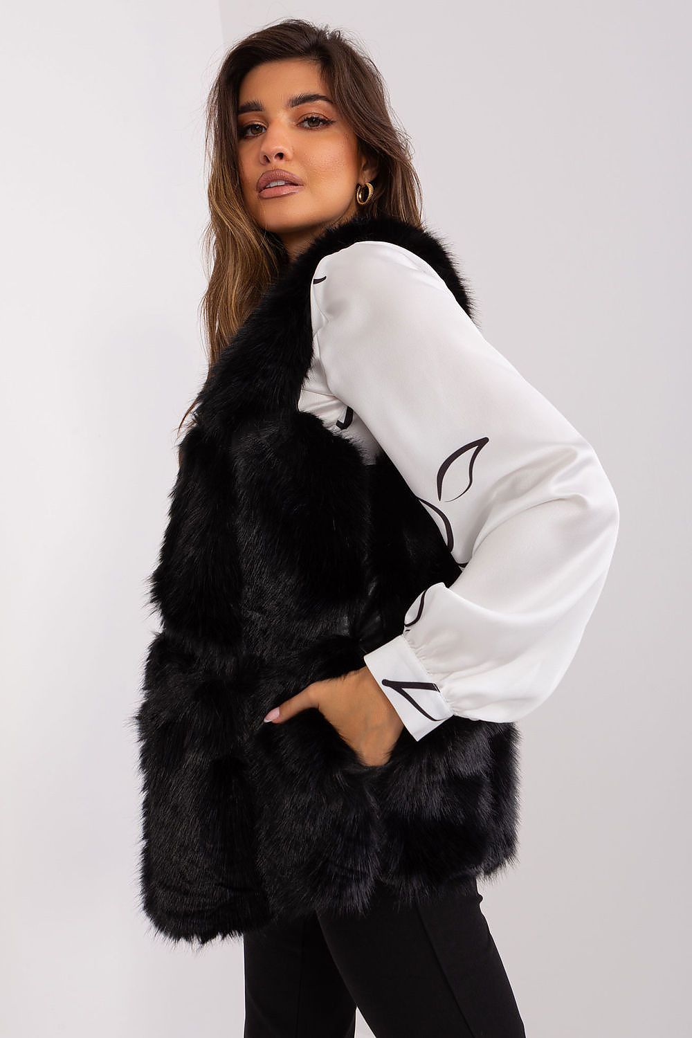 Woman wearing a black fur vest over a white shirt on a plain background