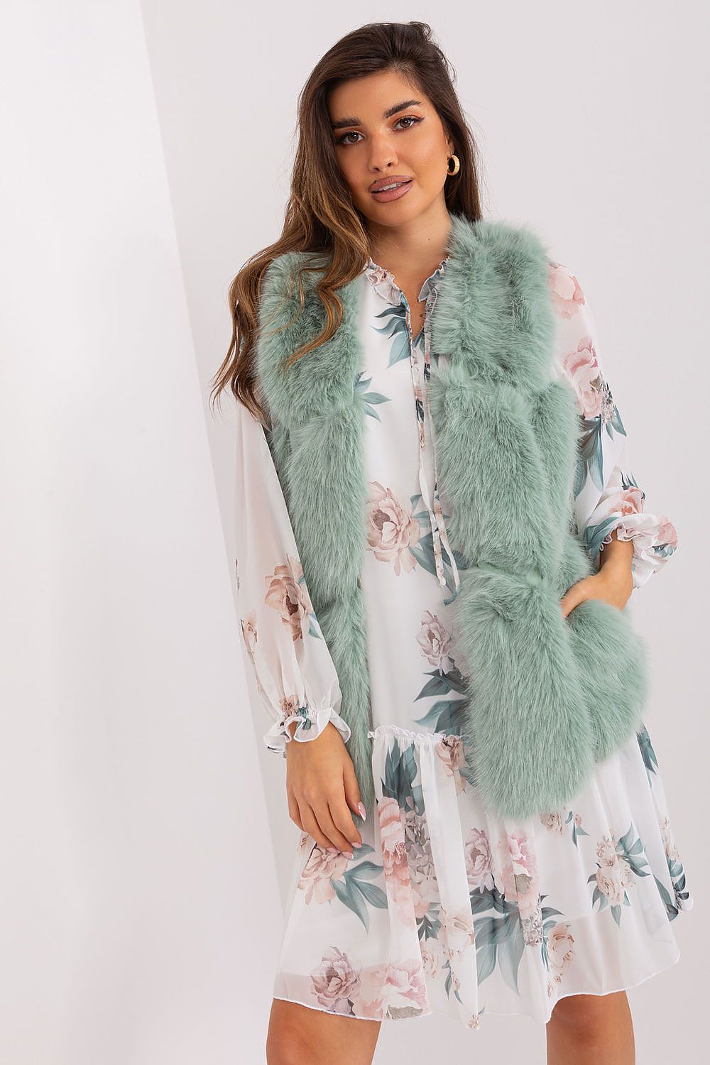 Woman wearing a light green fur vest over a floral dress on a white background