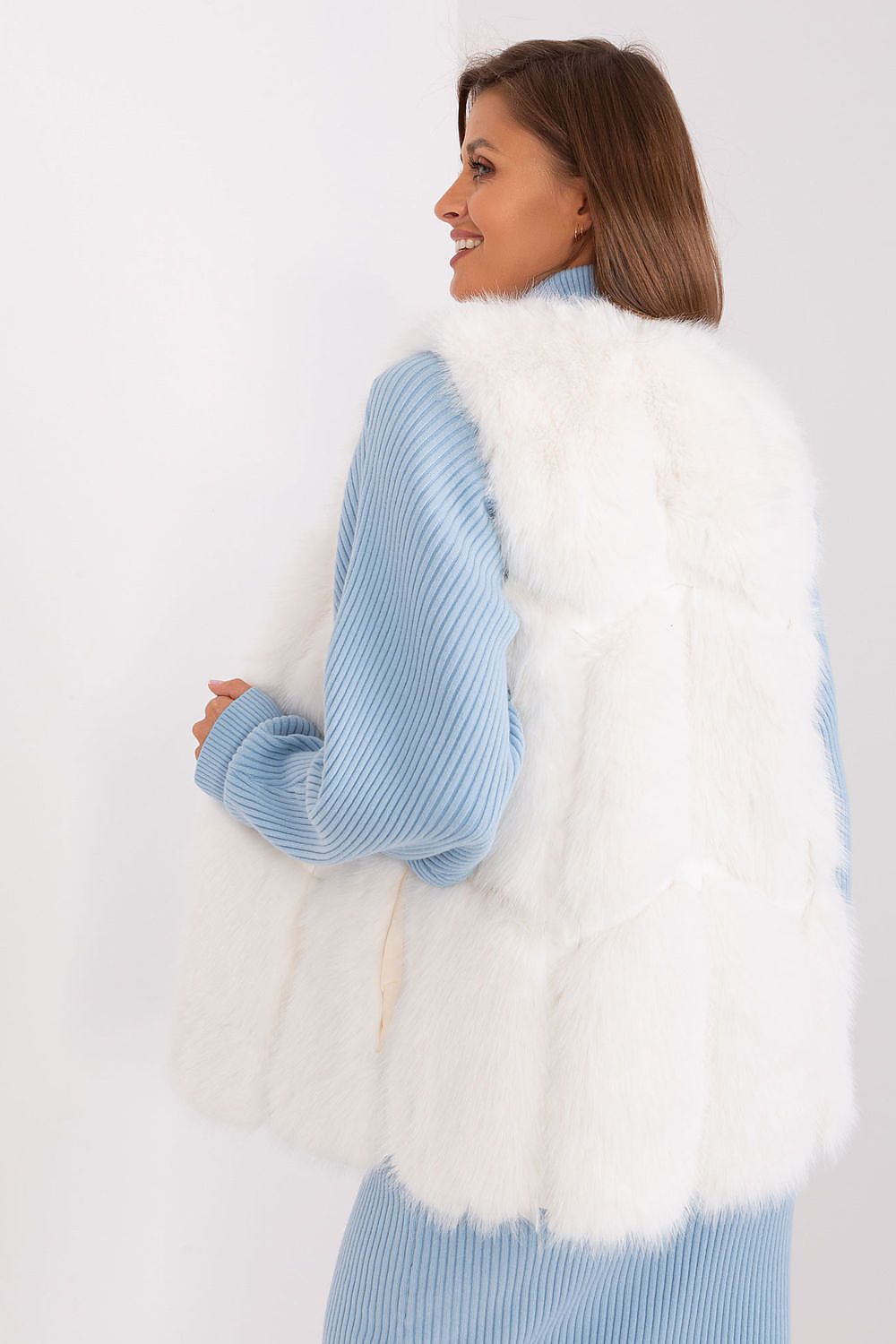 Woman wearing a light blue sweater and white fur vest against a white background