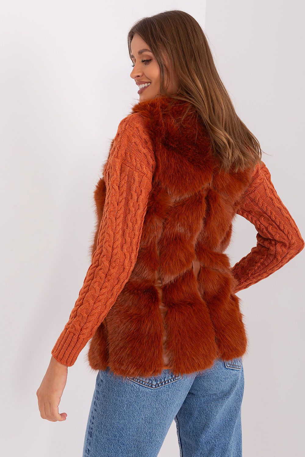 Woman wearing a rust-colored knitted sweater with a fur vest on a white background