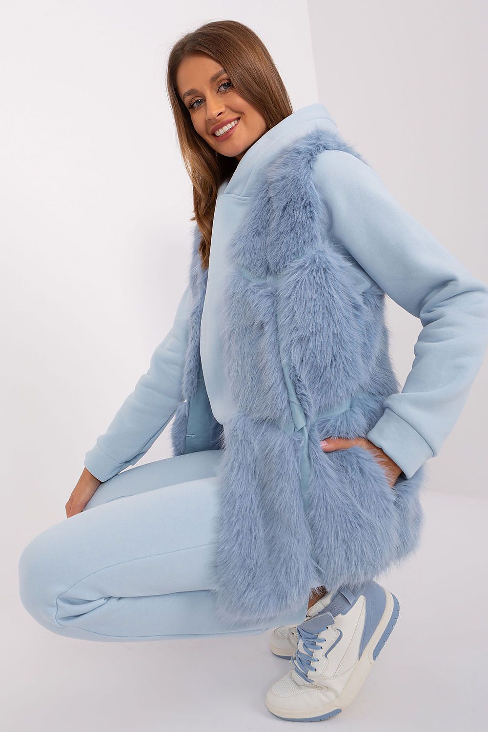 Woman wearing a light blue outfit with a fluffy vest on a white background