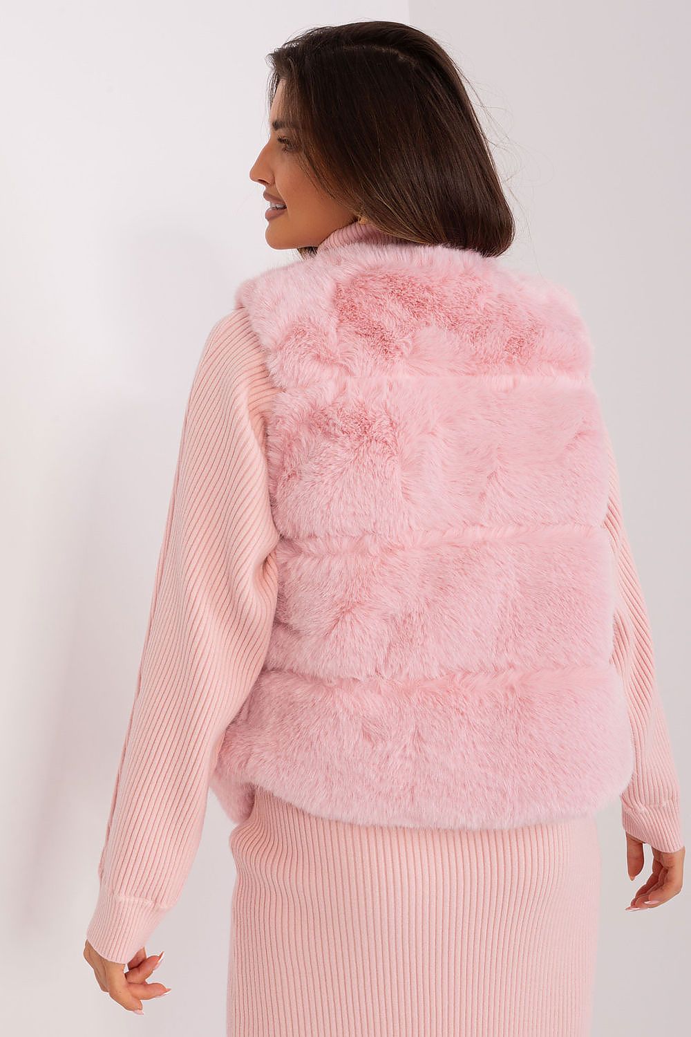 Woman wearing a pink fluffy vest over a matching pink sweater on a white background