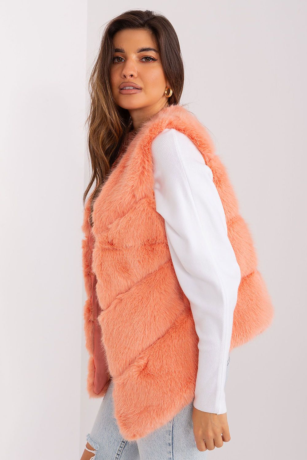 Woman wearing a coral pink faux fur vest over a white shirt on a plain background