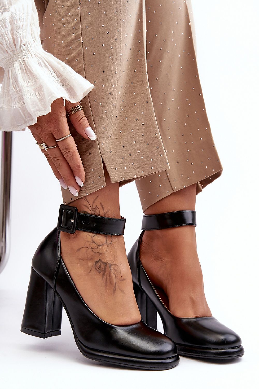 Black high-heeled shoes worn with beige pants on a white background