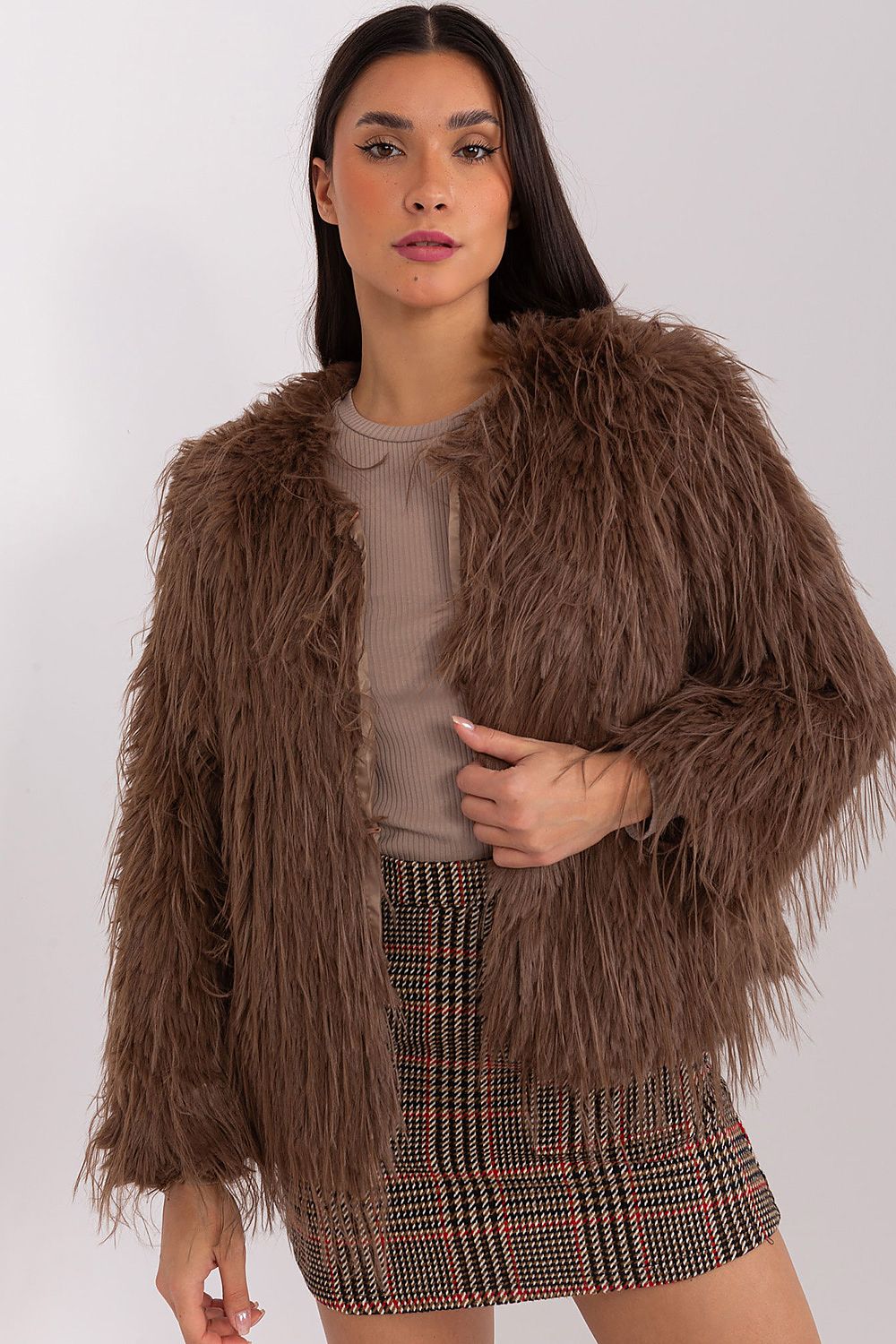 Woman wearing a brown fluffy jacket and plaid skirt on a white background
