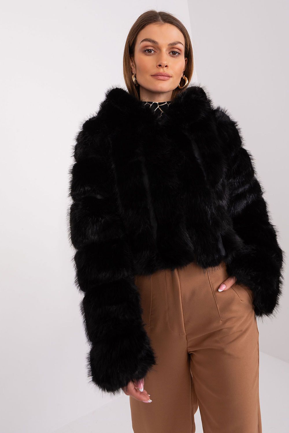 Person wearing a black fur coat and brown pants on a white background