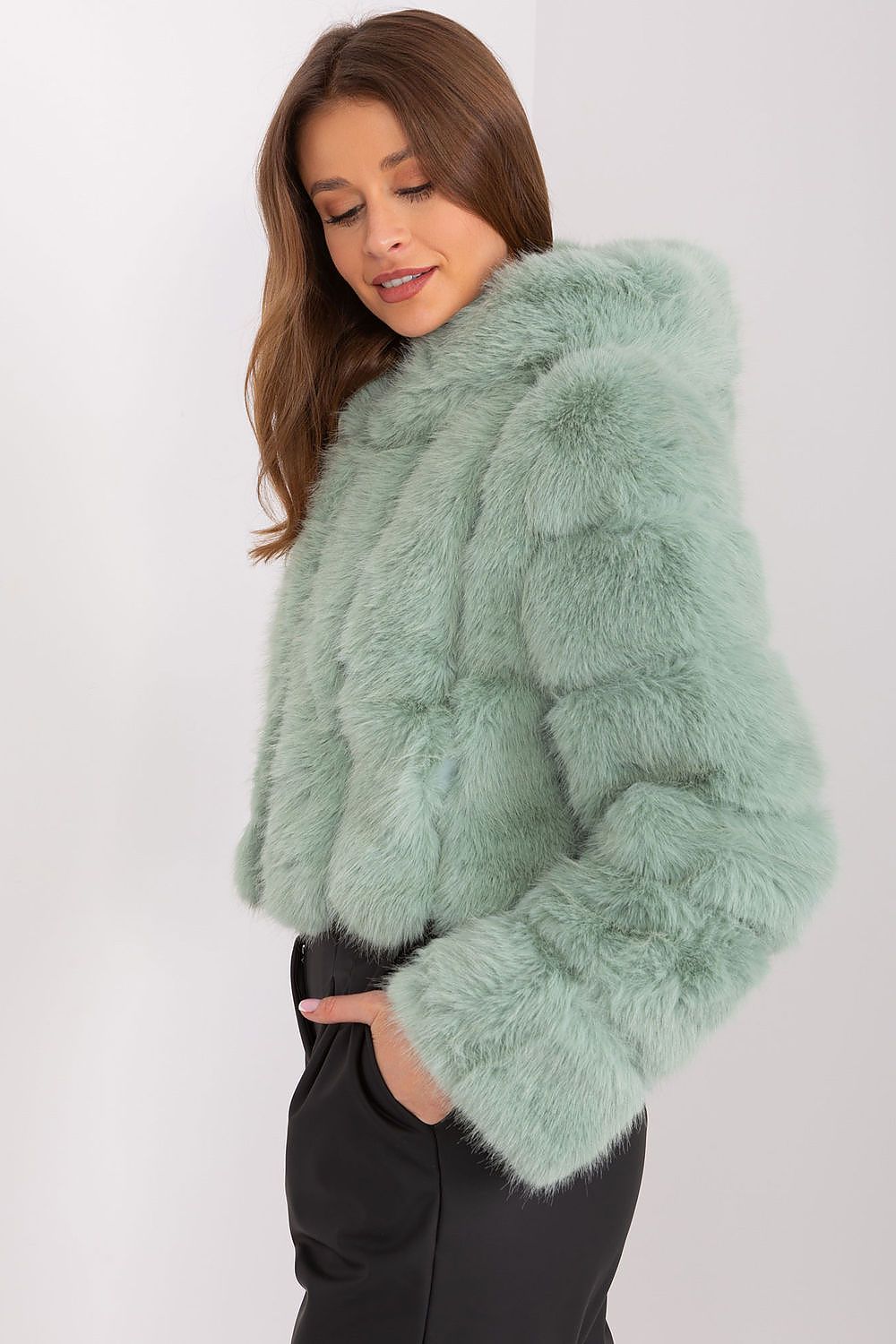 Woman wearing a light green fur coat against a white background