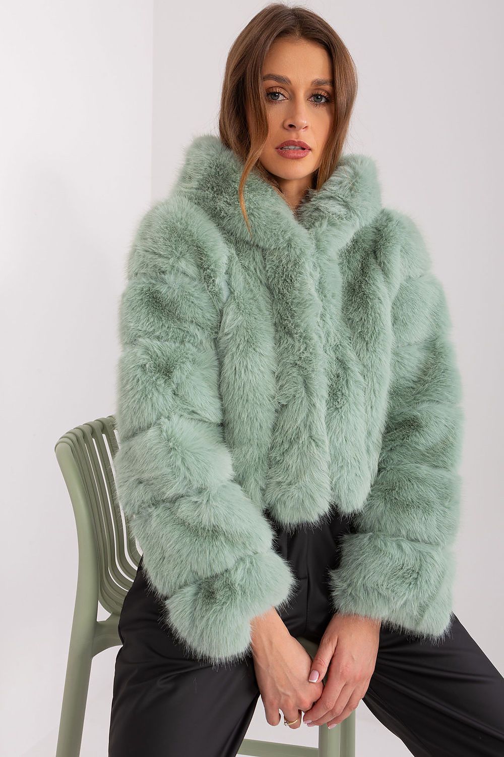 Woman wearing a light green fur coat sitting on a chair against a white background