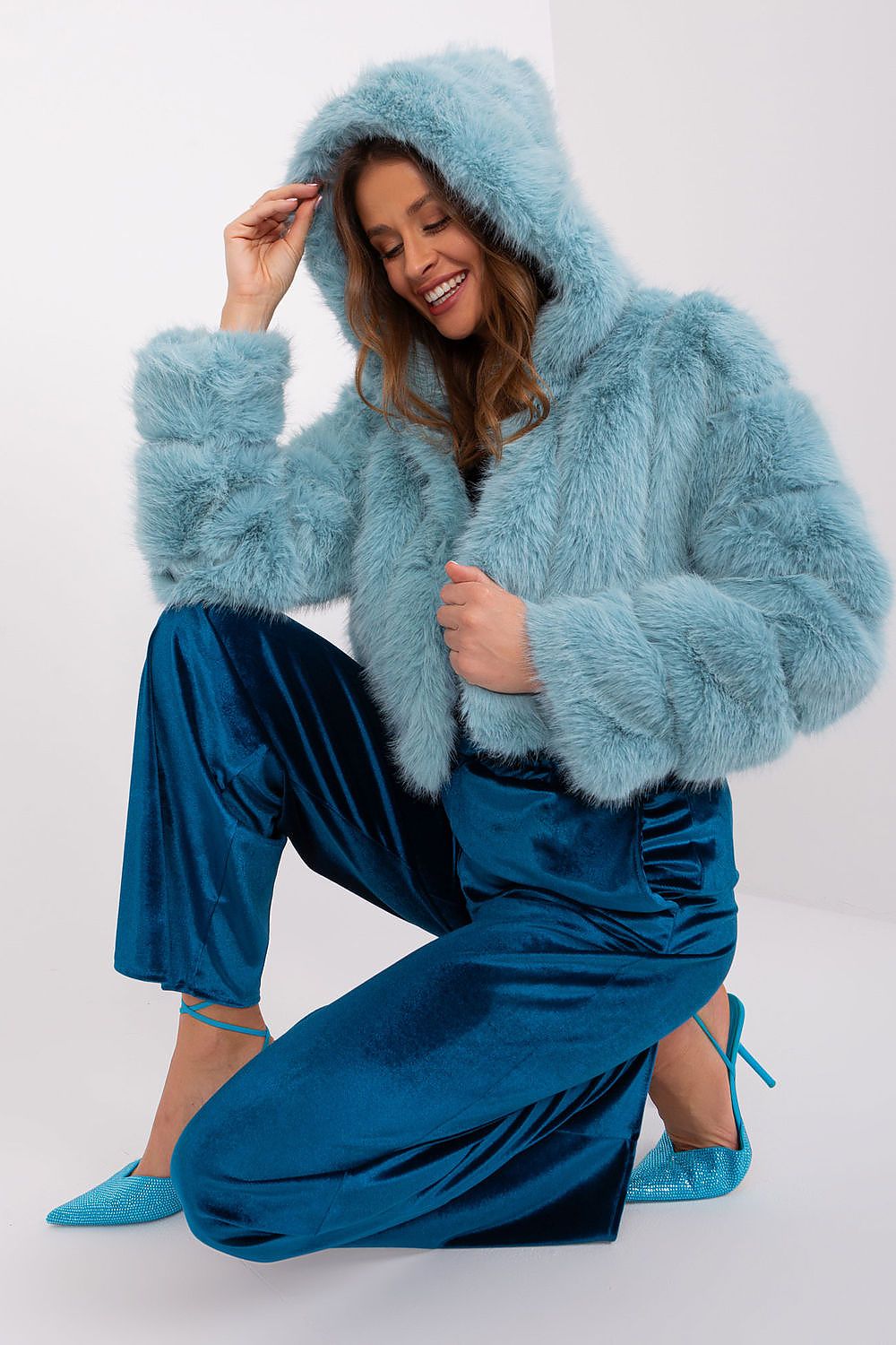 Woman wearing a light blue fluffy jacket and blue pants on a white background