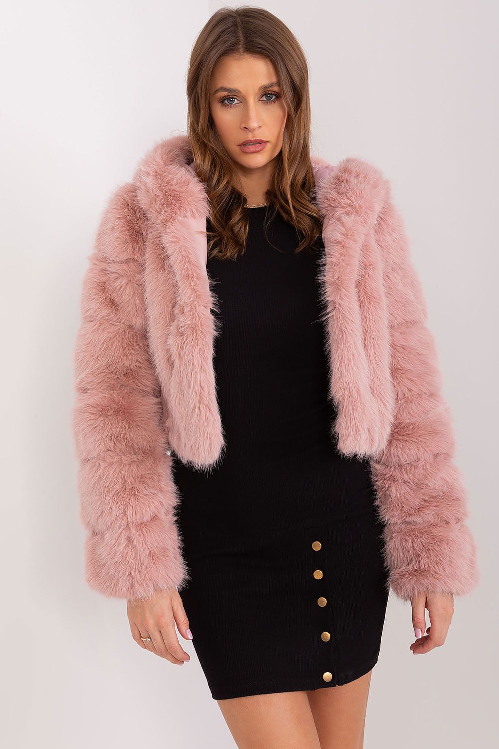 Woman wearing a pink fluffy jacket over a black dress with gold buttons on a white background