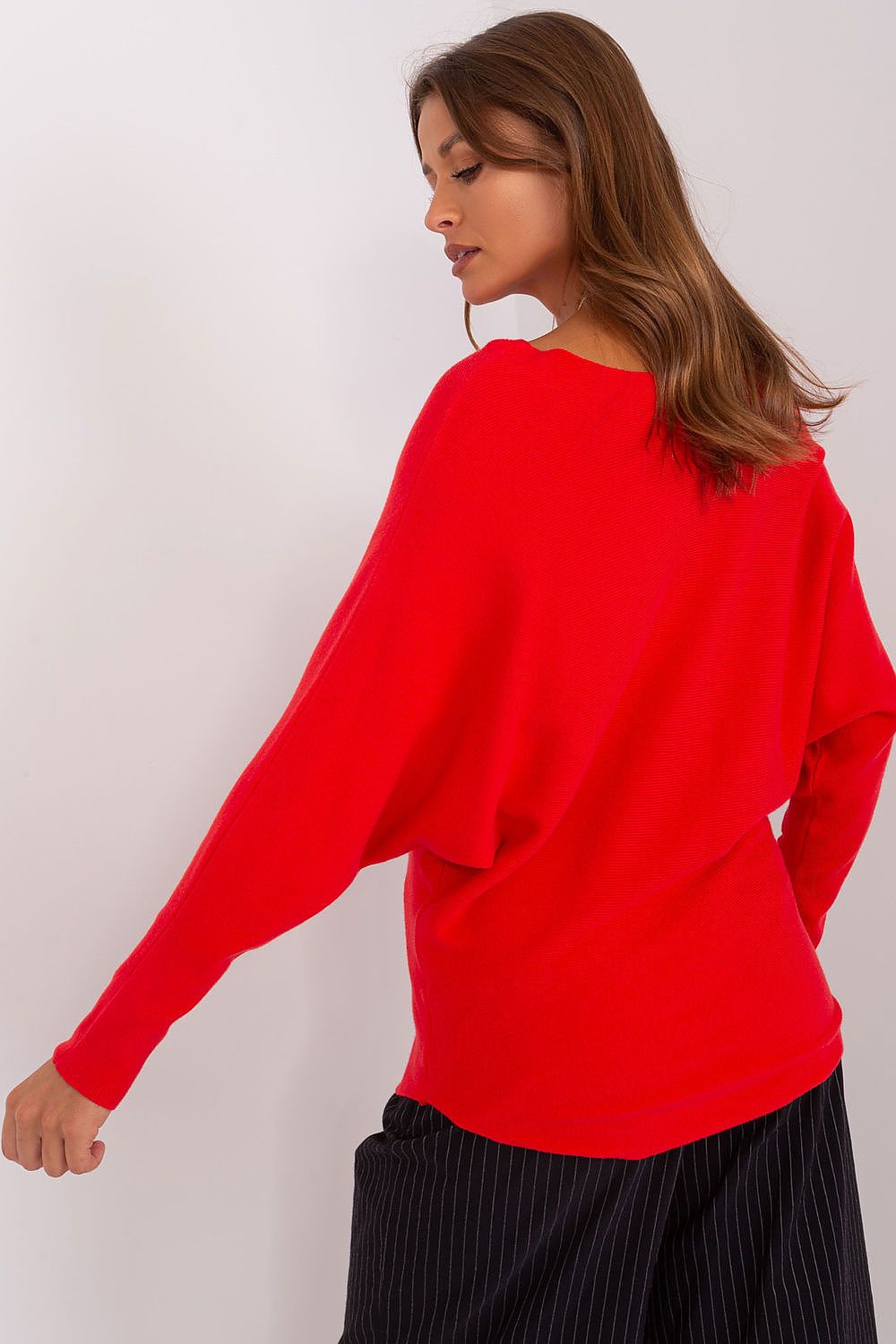 Woman wearing a red sweater and black pleated skirt on a white background