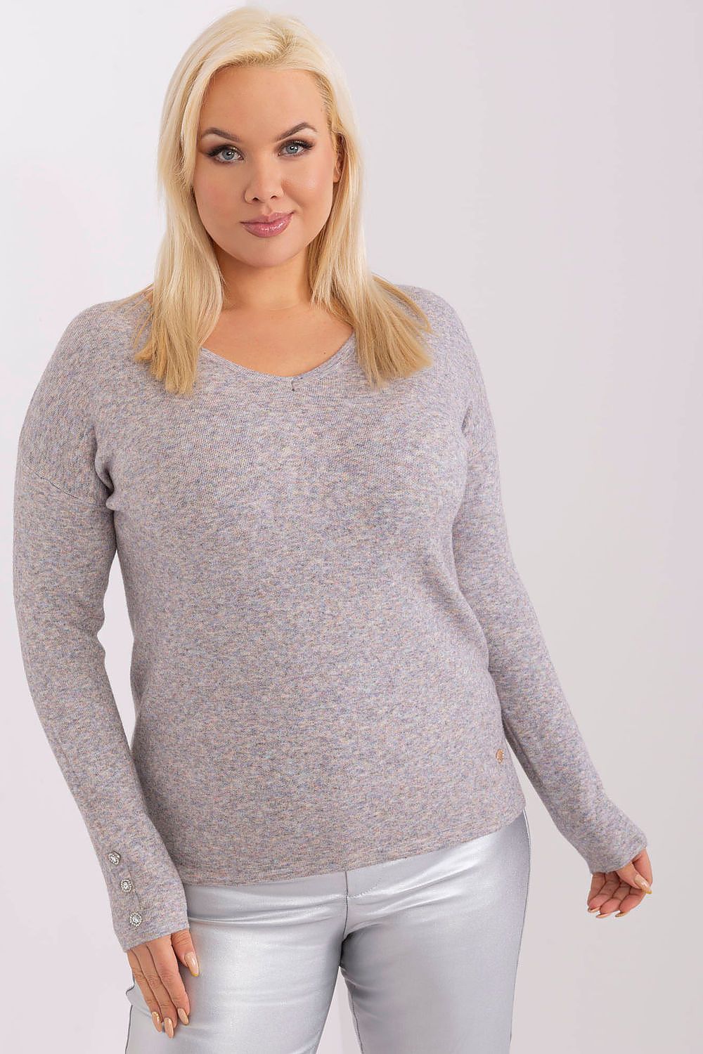 Woman wearing a gray sweater and white pants on a plain background