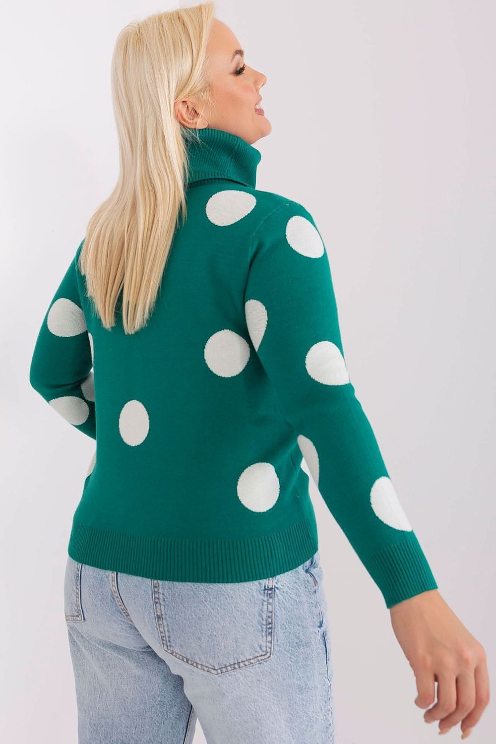 Woman wearing a green sweater with white polka dots on a plain background