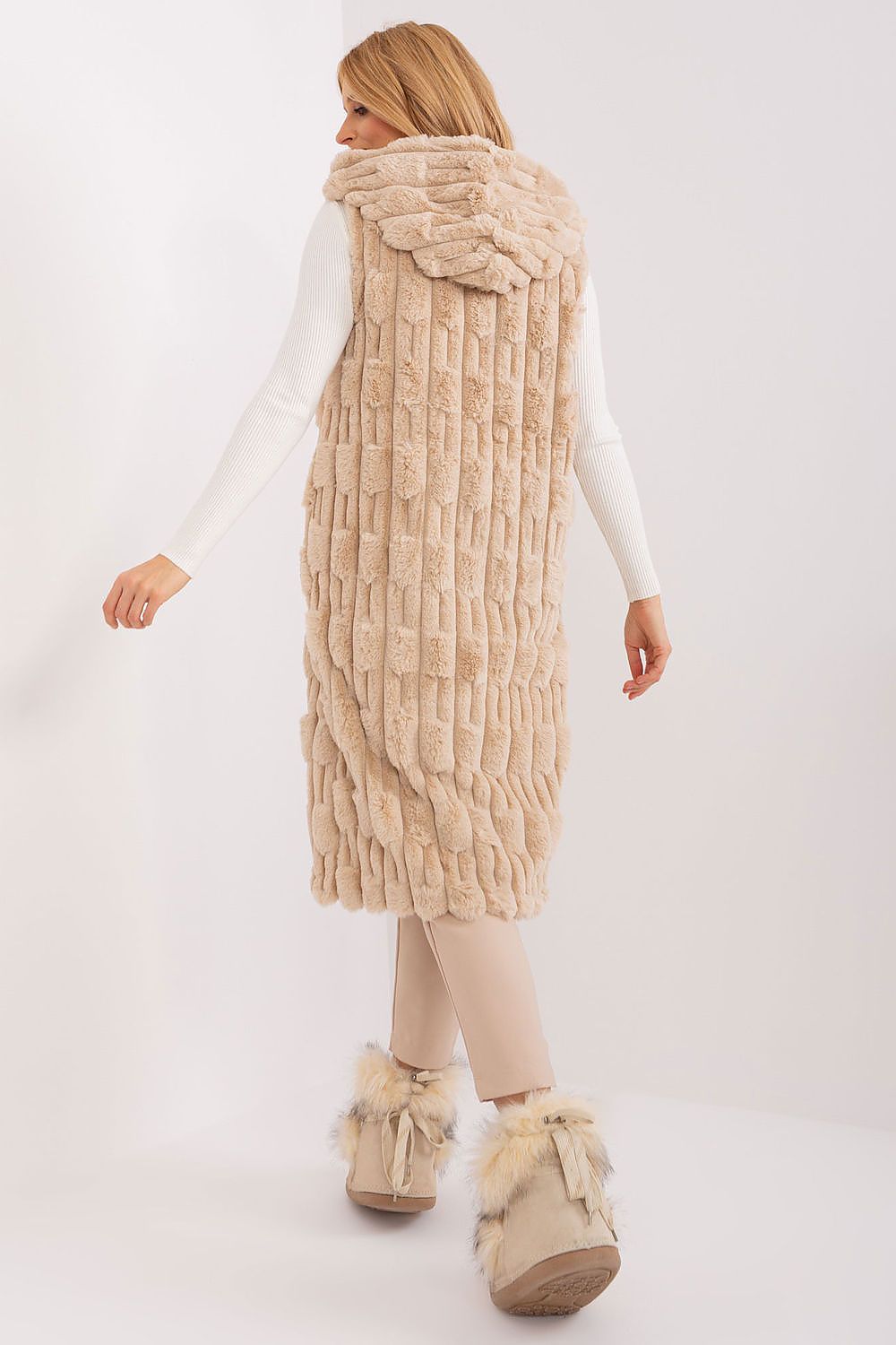 Woman wearing a beige knitted vest and matching boots on a white background